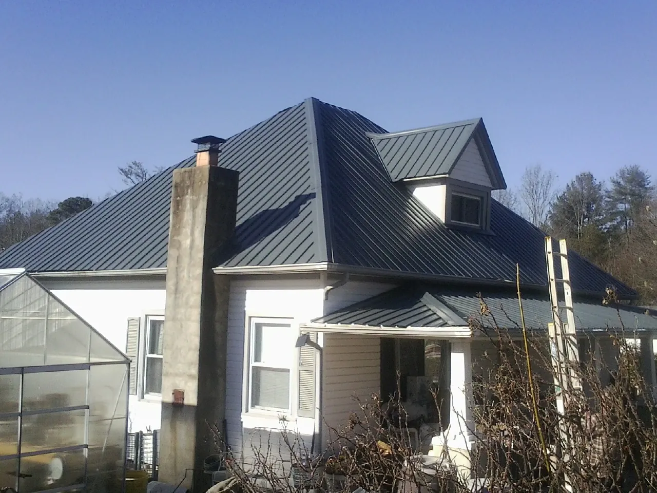 Dark blue standing seam metal roof on a white farmhouse with dormer — Slate & Tile Roof Repair by Roofing Brothers in Malverne