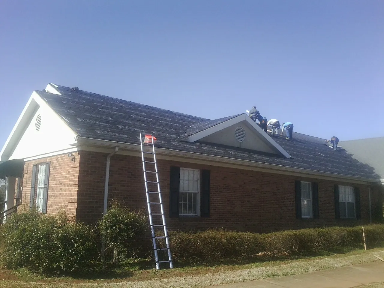 Crew tearing shingles off a brick ranch roof with a ladder set — Metal Roof Repair work by our crew in Malverne