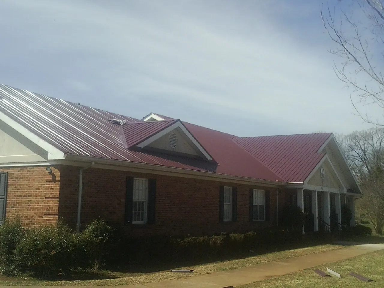 Red metal roof with gabled entries on a long brick building, from a Hail Damage Roof Repair job in Malverne