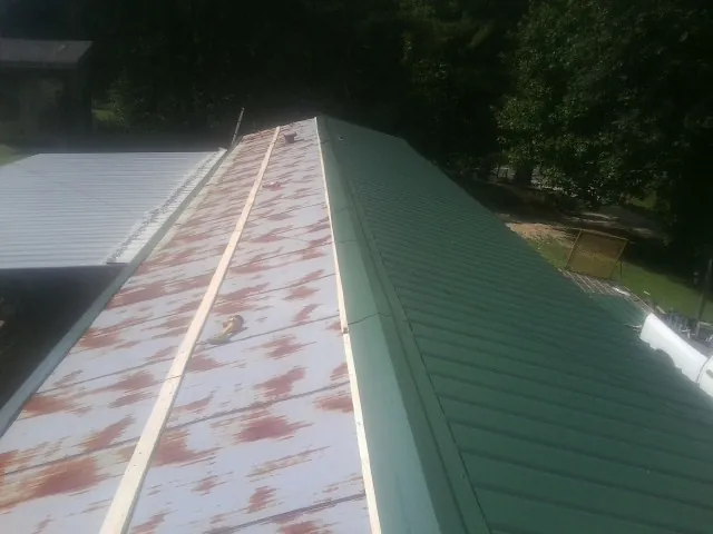 Old rusted panels beside newly installed green metal roofing — Wind Damage Roof Repair by Roofing Brothers in Malverne