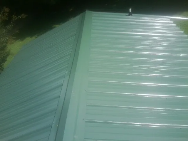 New green metal panels meeting at the ridge of a roof — Flat Roof Repair work by our crew in Malverne