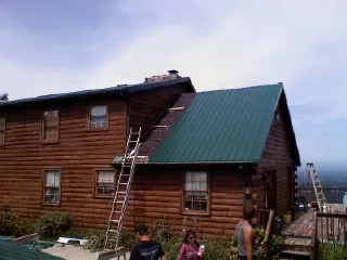 Green metal roof going on a two story log home with ladders set in Malverne