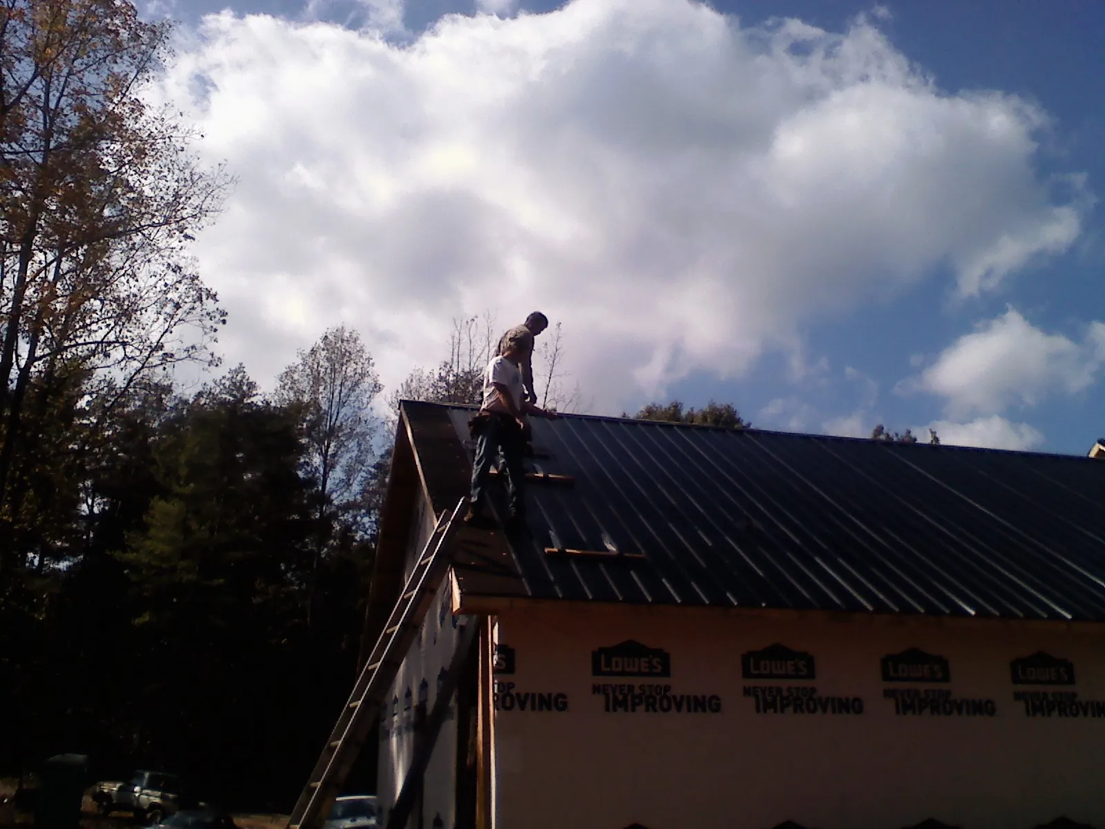 Roofer fastening dark metal panels high against a cloudy sky, from a Roof Inspection job in Malverne