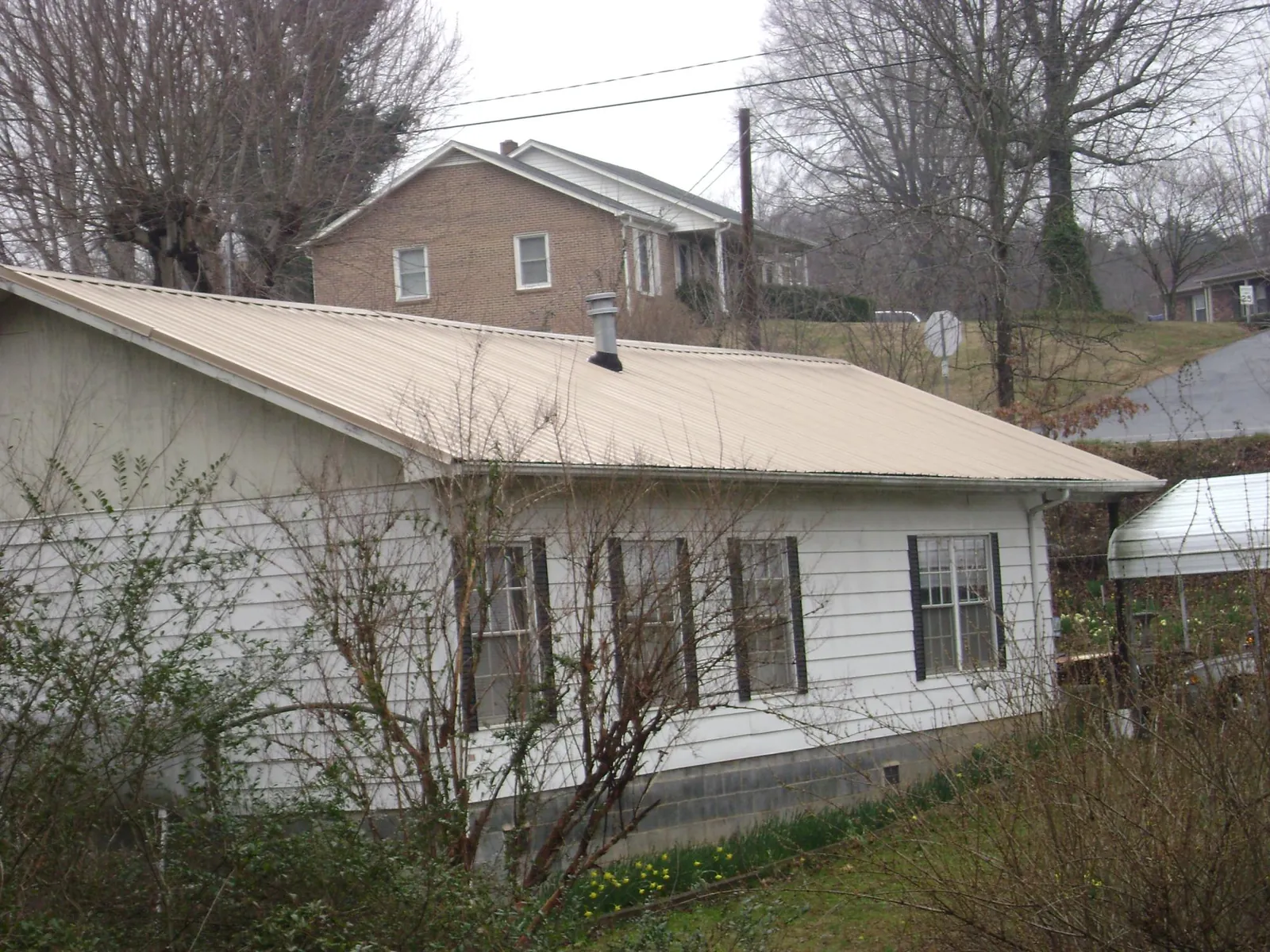 Tan metal roof on a white sided house set into a hillside — Commercial Roofing by Roofing Brothers in Malverne