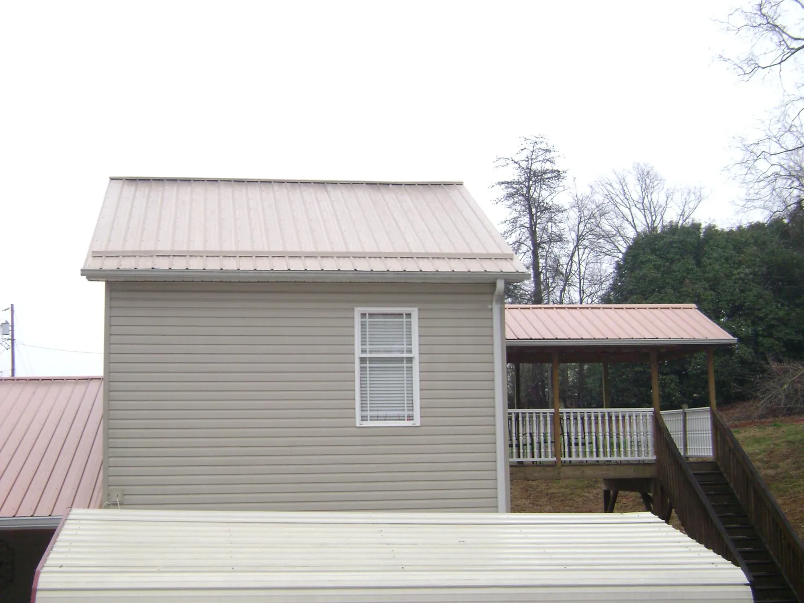 Tan metal roofs on a two story addition and attached porch, from a Roof Replacement job in Malverne